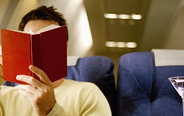Man reading book, being served martini, in first class on airliner